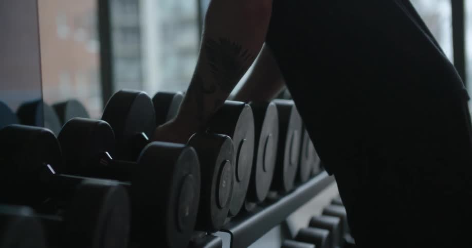 Man picking up two hand sized barbells from a rack filled with many of them