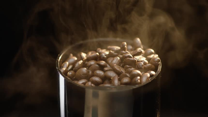 Close up of steaming hot coffee beans dropping inside a cilindrical metallic container