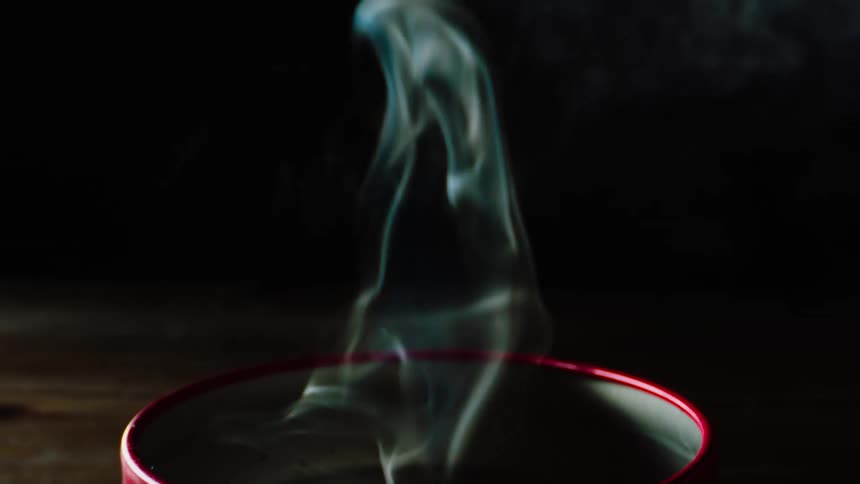 Wisps of smoke twist and turn in the darkness as they rise from a candle in a red container