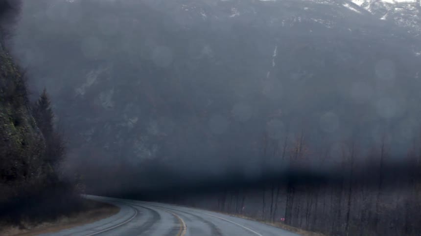 A vehicle drives on a mountain road while it rains