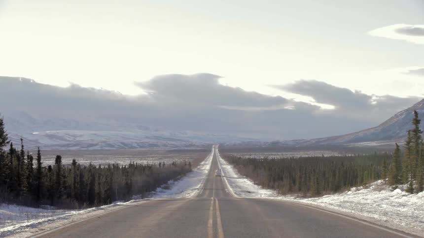 A semi-truck drives on a wilderness road in the winter