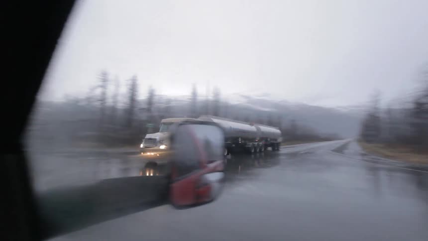 A vehicle passes by a semi-truck on a rainy day