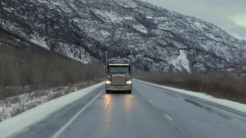 A semi-truck drives on a mountain road in the winter