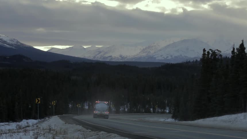 A semi-truck drives on a mountain road in the winter