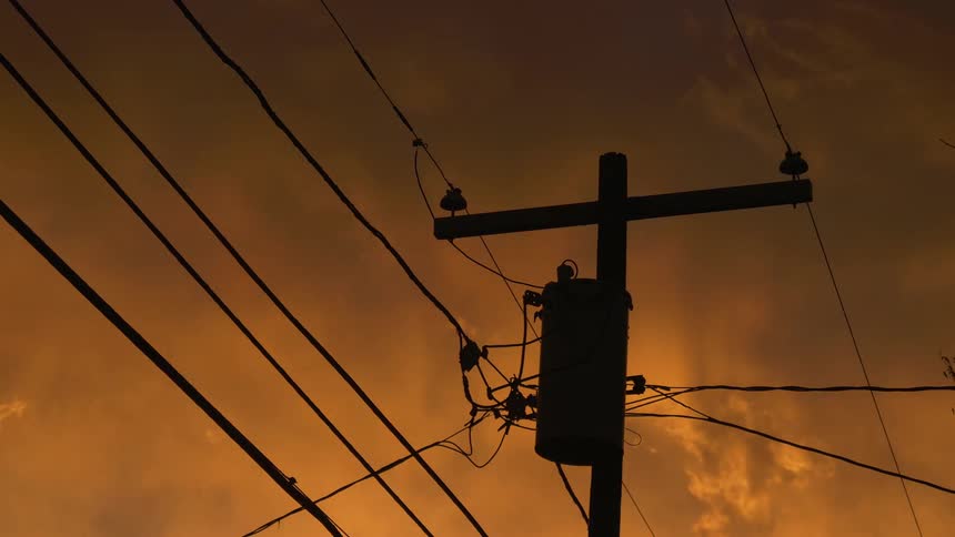 The setting sun turns the sky orange behind a utility pole