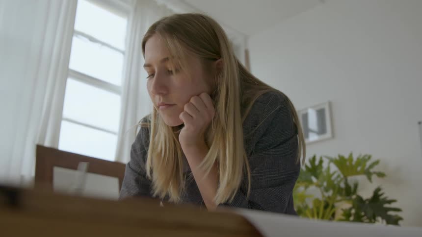 Blonde woman writes at table before turning to look behind her