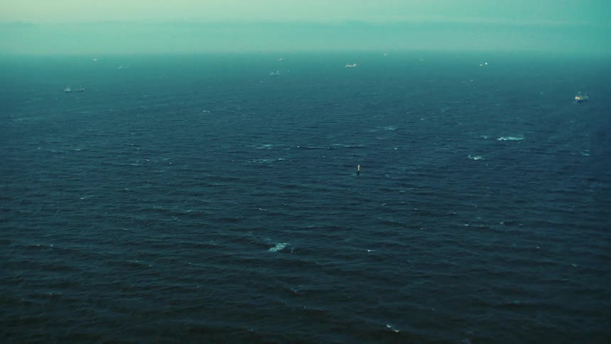 Small waves ripple over the ocean a few large ships are barely visible