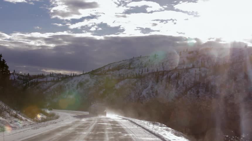 Vehicles are traveling down a winding road near a mountain