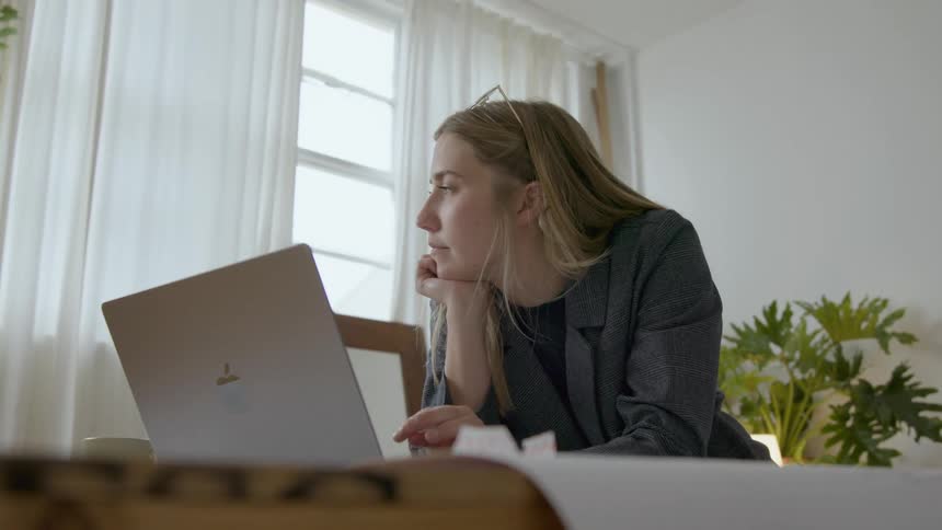 A blonde woman deep in thought while hunched over a laptop