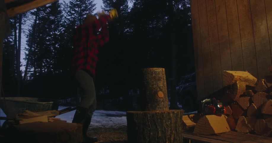A man using an ax to chop wood at blue hour in winter