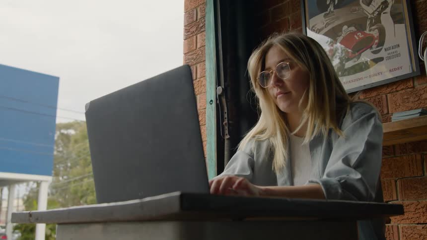 A blonde woman putting on glasses and typing on a laptop