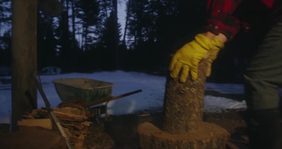 A man in a red flannel shirt chopping wood on a cold winter evening
