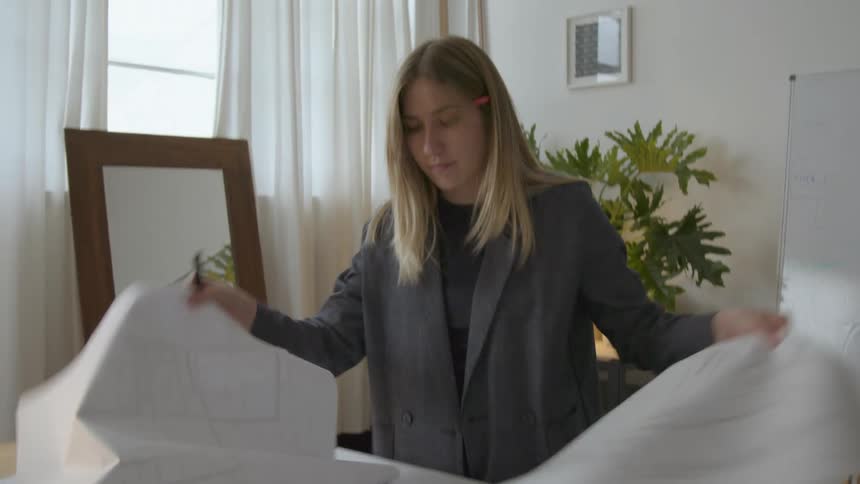 A woman is standing over a table as she looks through sketches on large paper