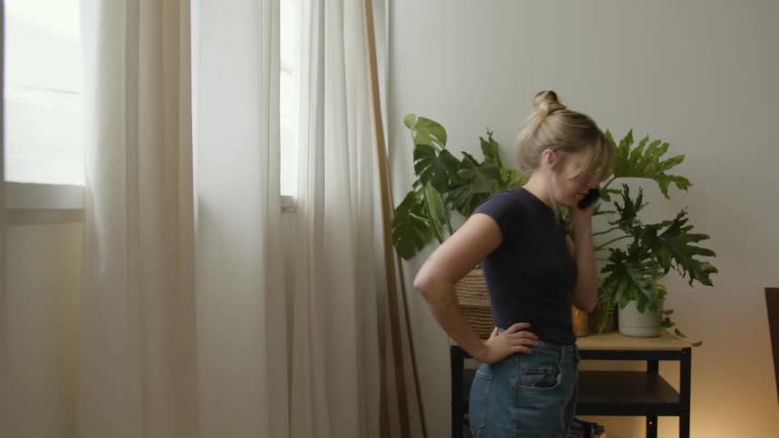 Woman place mug on window sill then paces back and forth while talking on the phone