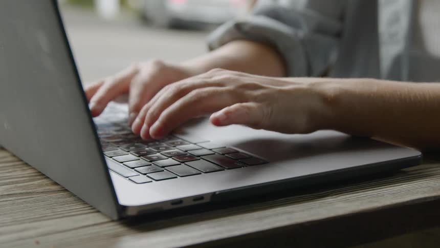 A person energetically writing on a laptop over a table finish with a flourish
