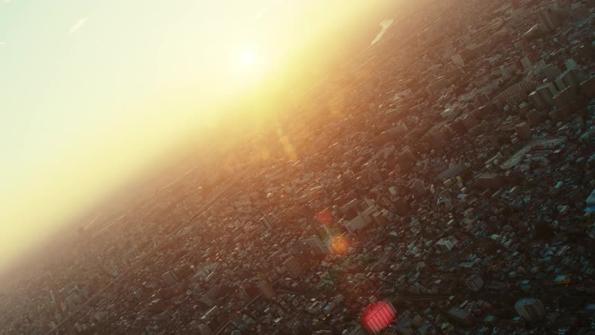 The sun shines brightly filling the hazy sky over a city filled with buildings and a river running through it