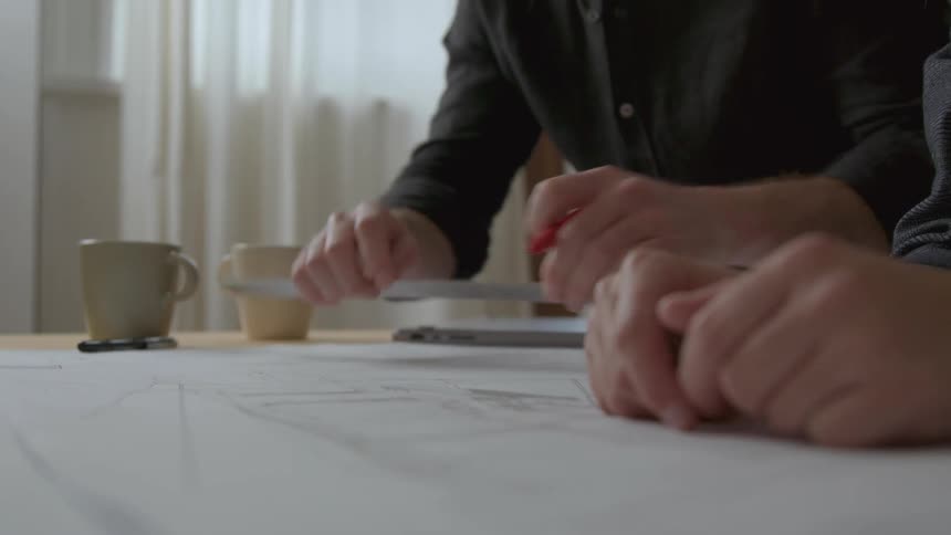 Couple of designers drawing construction blueprints over a desk in the office