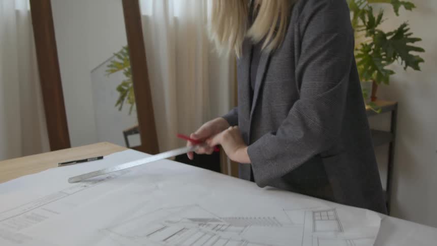 Young blonde woman drawing construction blueprints on a desk in her office