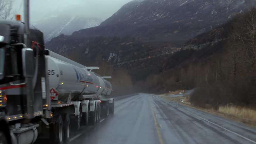 A semi-truck drives in the mountains during a rainstorm