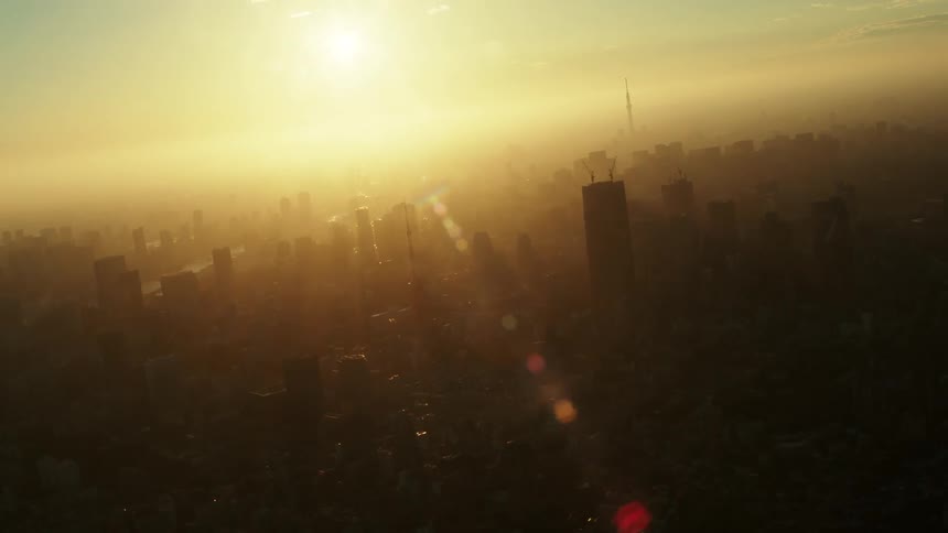 Twisting aerial footage of a large metropolitan area skyline covered in fog or smog at sunset