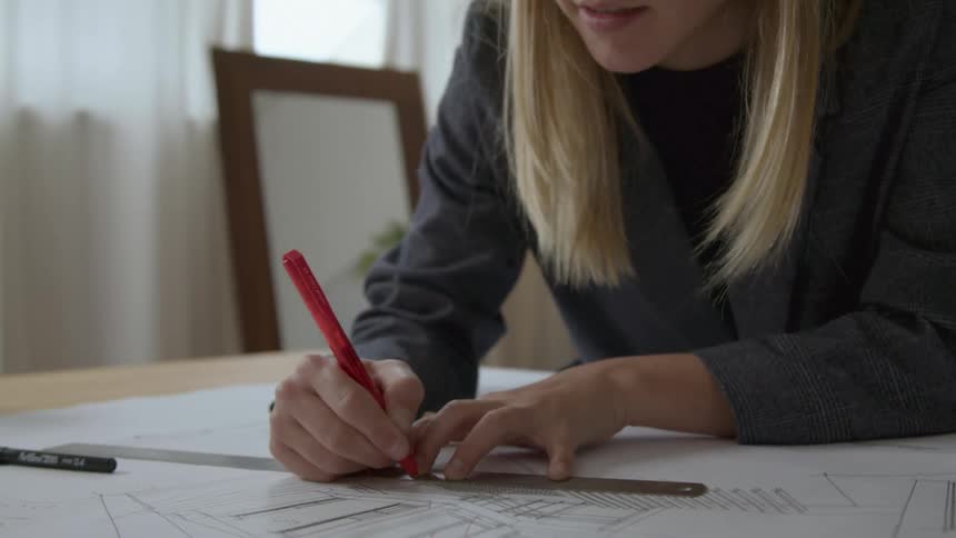 A woman is sitting at a table drawing plans with a ruler
