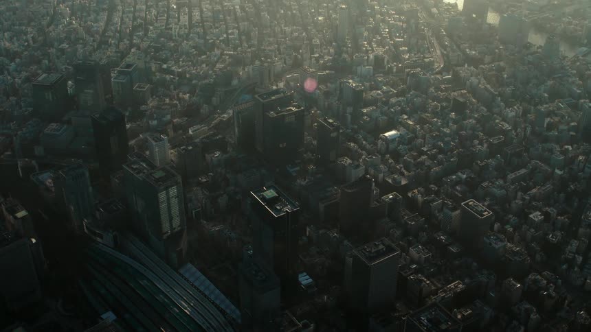 Roads are near tall towers in a crowded city as the sun shines on a hazy sky