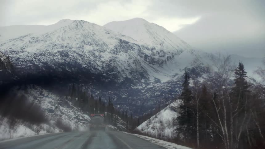 Snowy mountains as seen from behind a windshield with the wipers cleaning it