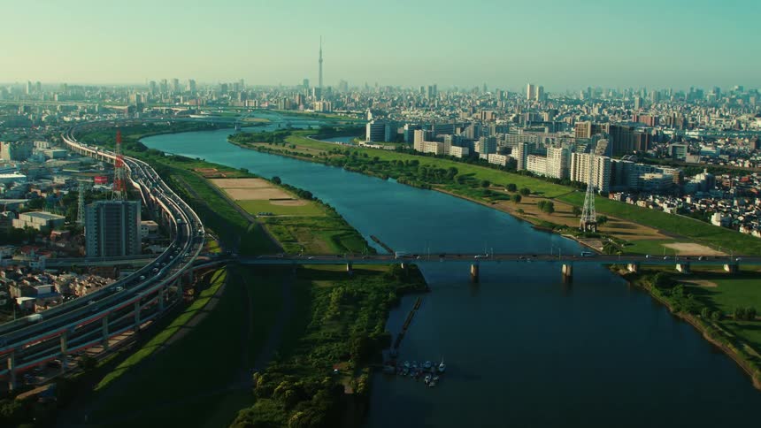 An aerial view of a river running through a city with office buildings and vehicles driving on roads and across a bridge