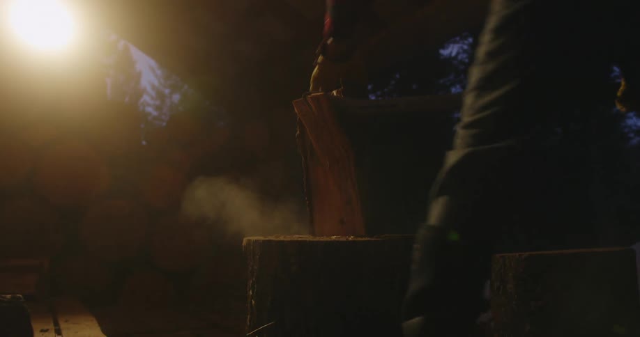A man is outside splitting wood with an ax at blue hour in winter