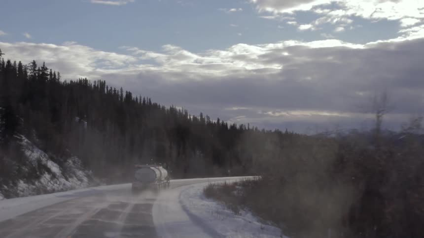 A semi-truck drives on a snowy mountain road