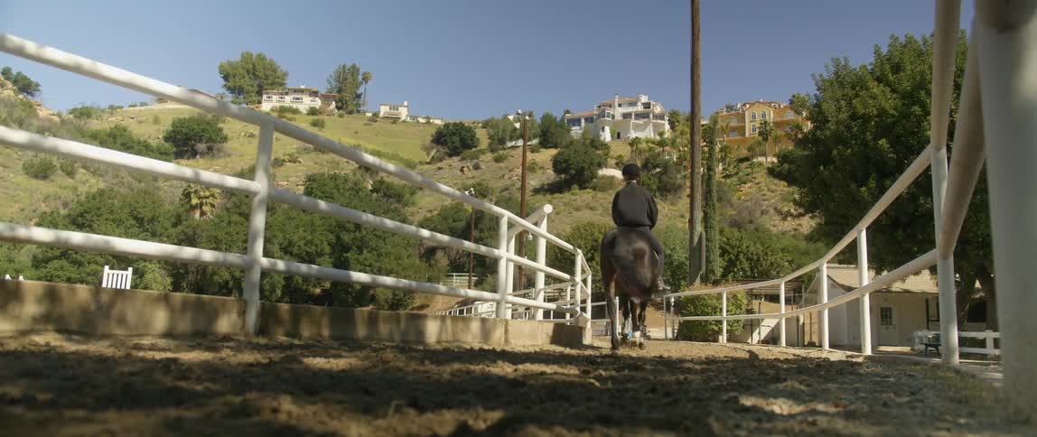 A person riding a horse next to white fencing