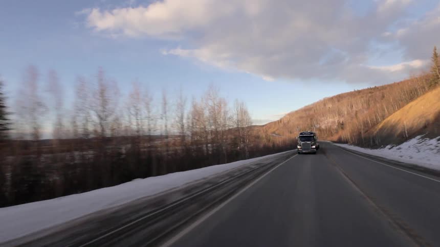 A semi-truck drives in a snowy and rural area