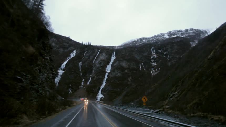 A semi-truck drives on a mountain road while it rains