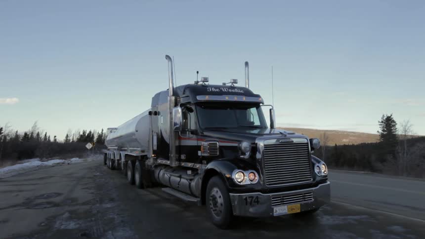 A truck hauling two tankers driving on a road with snow on the sides