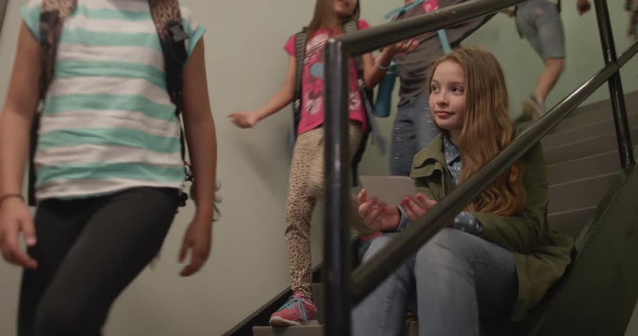 School children walk down stairs as one girl sits on the steps and reads a note