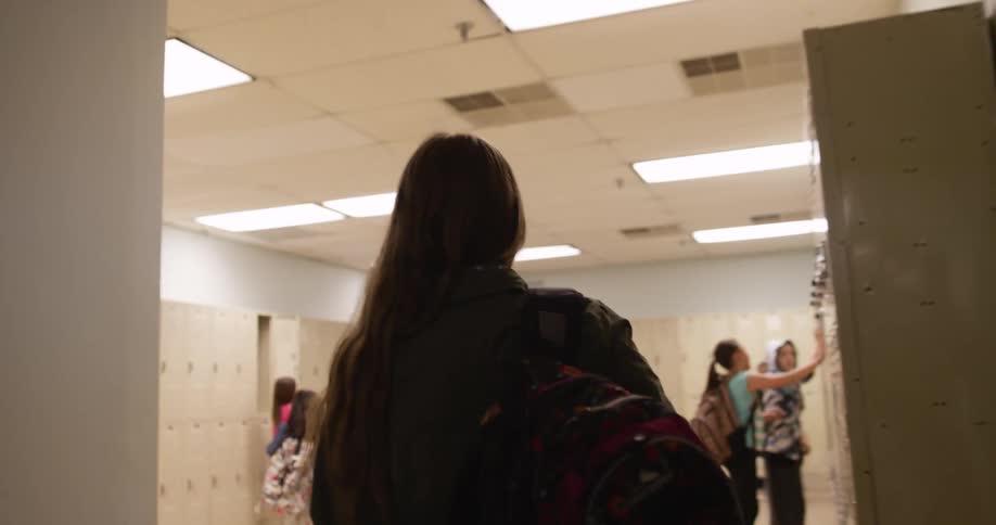 A girl wearing a backpack is walking through a school's corridors during the day