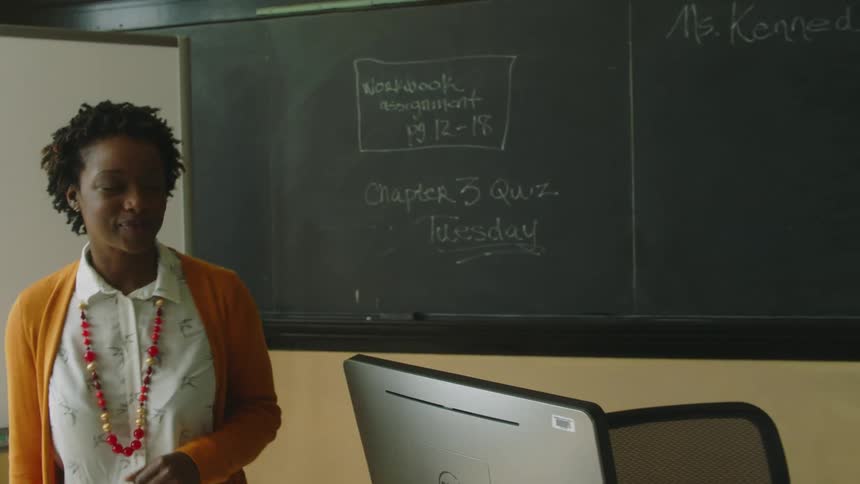 Student hands her teacher some papers in a classroom