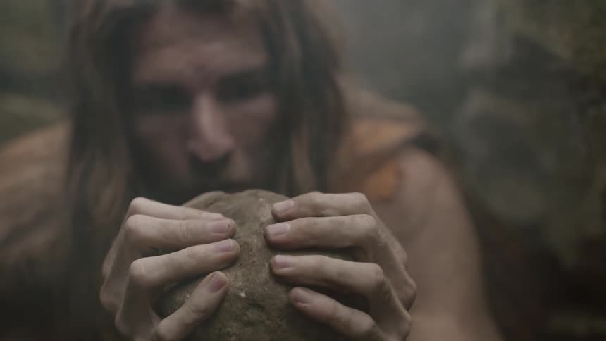 A caveman stares and and examines a rock as if he's never seen a rock before