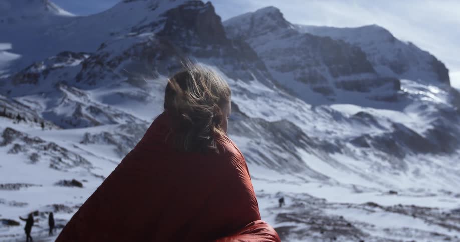 Woman standing in the snowy wilderness a red blanket covering her while it's blowing in the wind