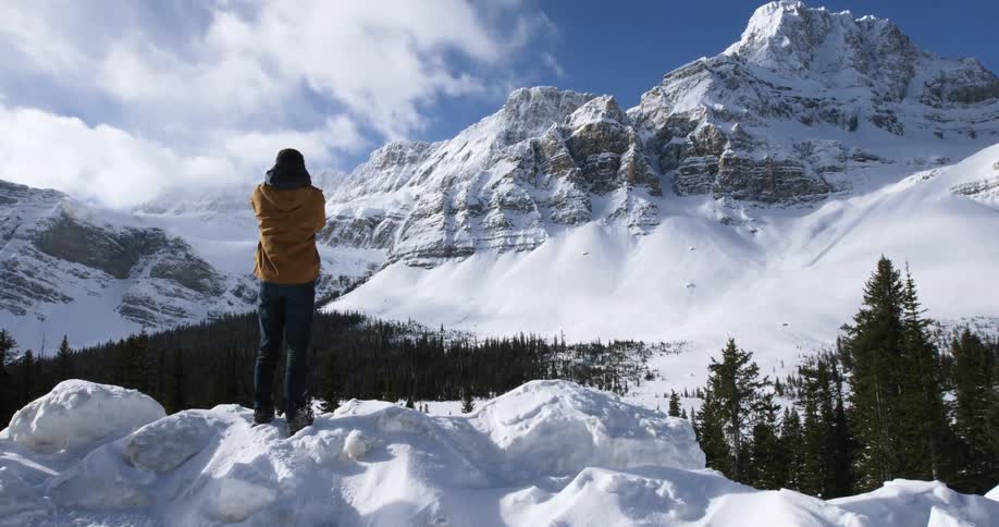 A man is standing on mounds of snow looking over at a mountain