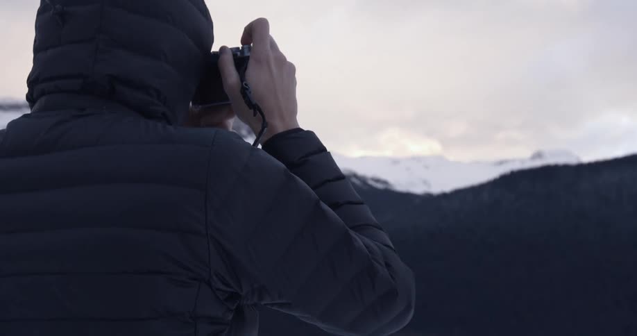 Hooded person taking photos of the wilderness in front of them on a cloudy day