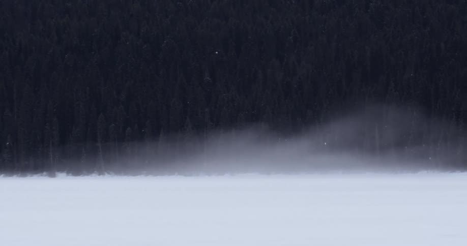 A large snow covered field leads to a hill covered with trees