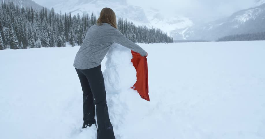 Woman putting her red jacket on freshly made snowman