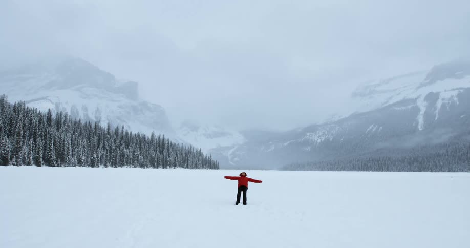 A woman standing in a snow covered valley falls backward into the snow