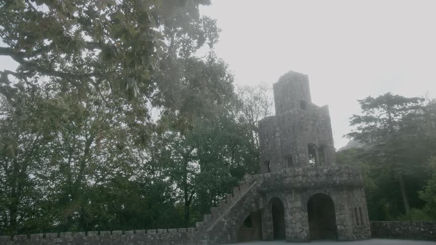 An old battlement tower stands amidst trees during the daytime