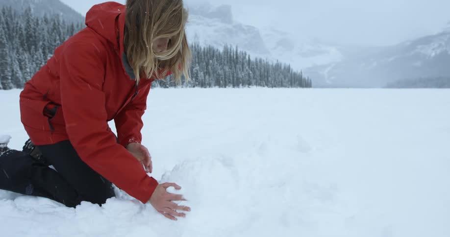 A woman is forming a snowman in the snow