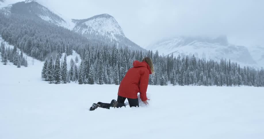 A woman rolls a large ball of snow in the mountains during a snowstorm