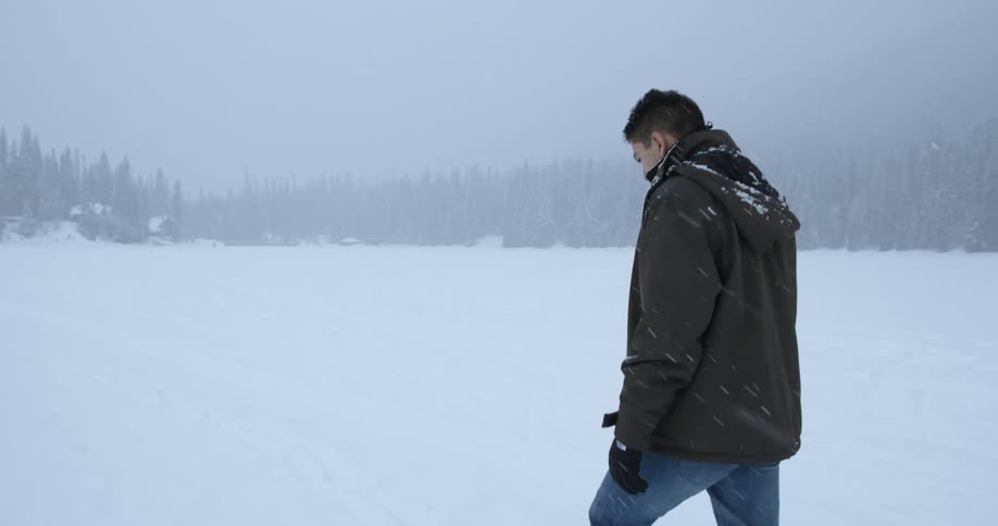 A man walking through a field as snow falls
