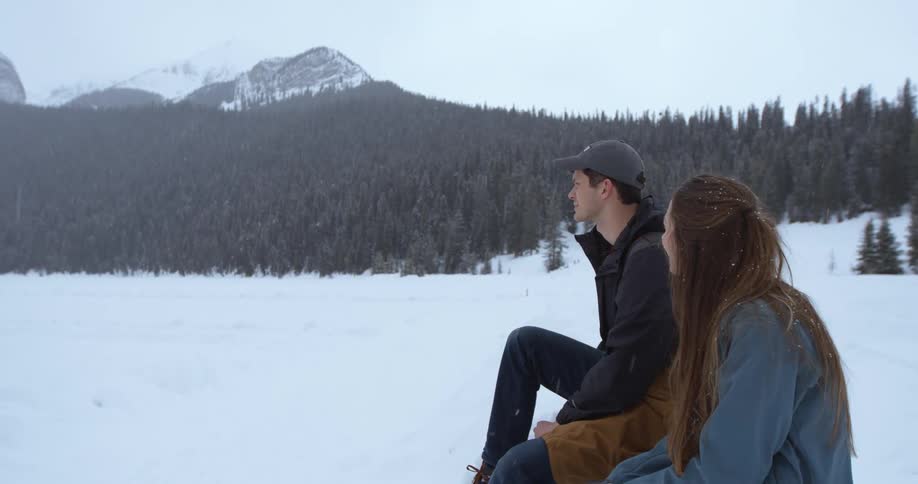 A man and woman sit down in the snow talking