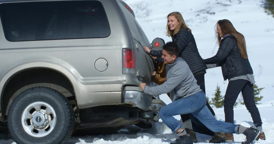 A group of people try to push a truck out of the snow